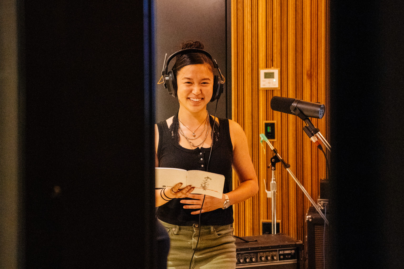 Student with headphones on standing in recording booth